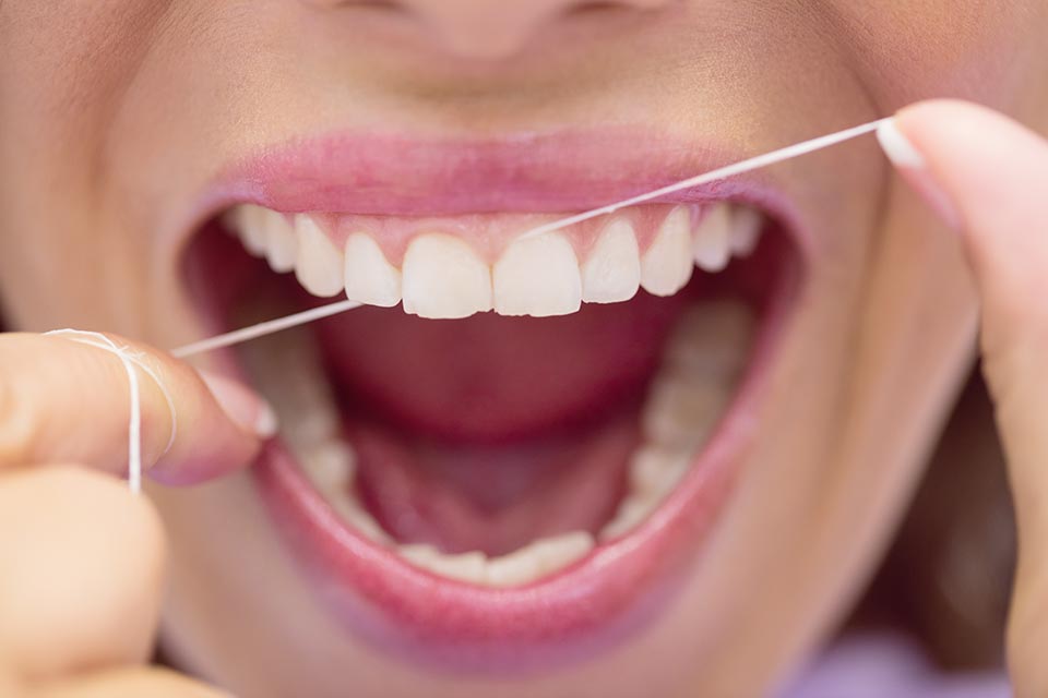 Mujer pasándose hilo dental entre dos dientes
